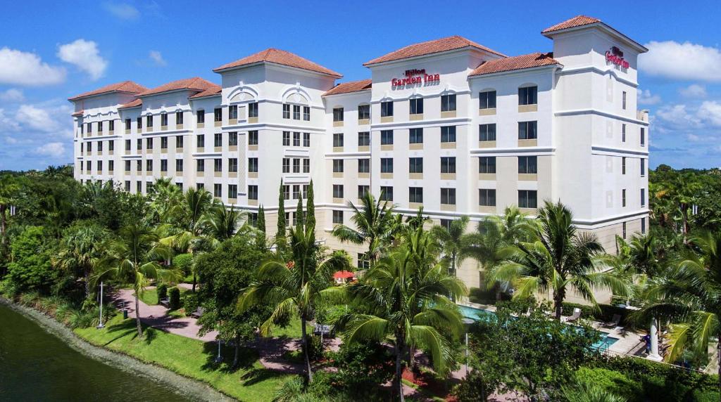 Hilton Garden Inn Palm Beach Gardens في بالم بيتش غاردن: مبنى ابيض كبير فيه نخل امام نهر