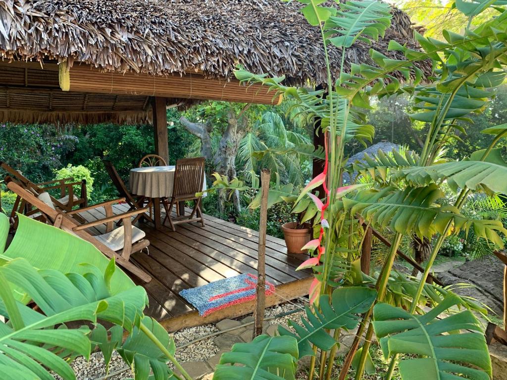 une terrasse en bois avec une table et un toit de chaume dans l'établissement Les Jardins d'Ankify, à Andimaka