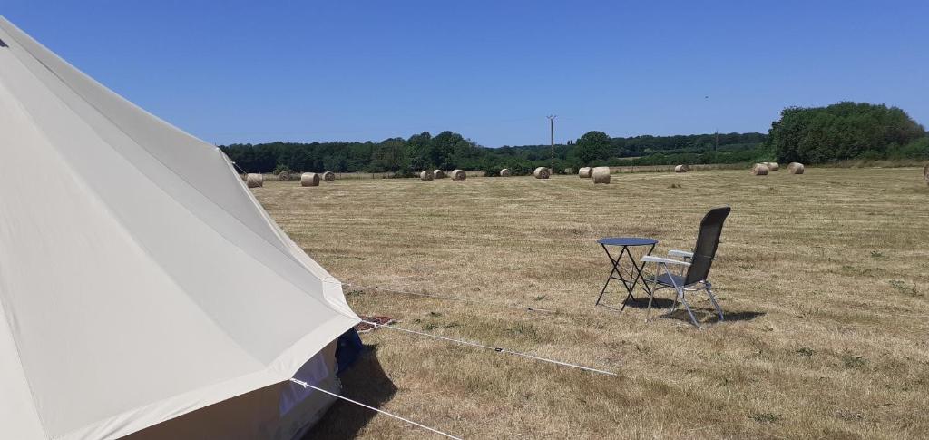 a tent and a chair in a field with hay bales at La tente saharienne du Perche .Chevaux. 