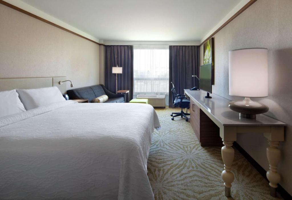 a hotel room with a bed and a desk with a lamp at Hilton Garden Inn Montreal Airport in Dorval