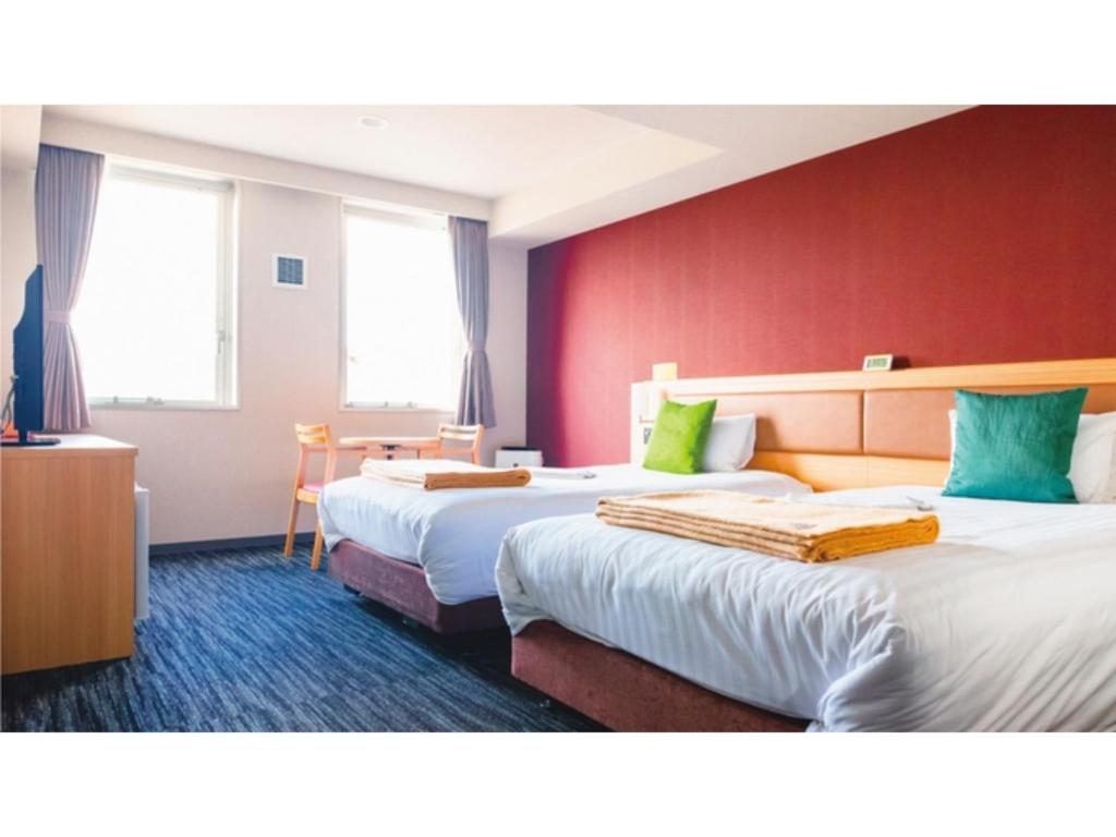 AIRAIKU HOTEL Kagoshima - Vacation STAY 17451v في Aira: سريرين في غرفة الفندق بجدران حمراء