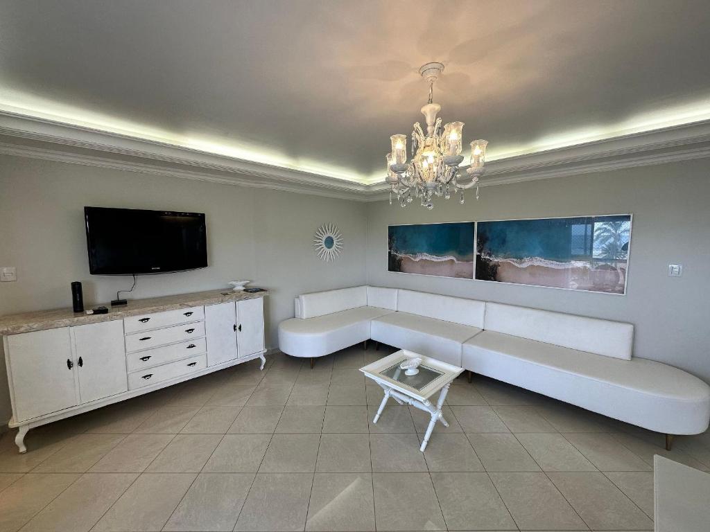 ein Wohnzimmer mit einem weißen Sofa und einem TV in der Unterkunft Frente Mar! 3 quartos e 2 vagas in Santos