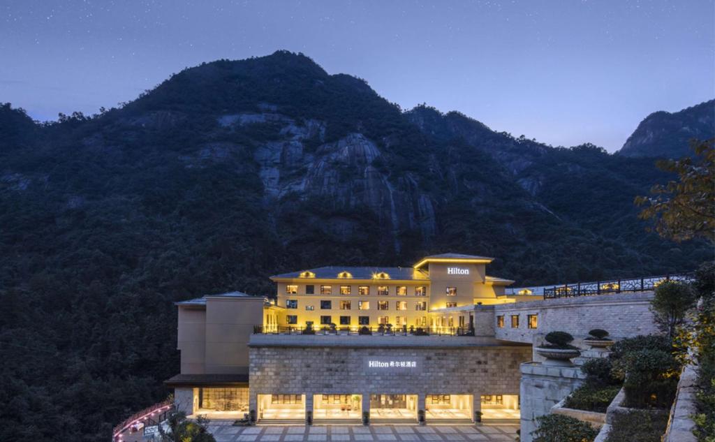 a building with lights on in front of a mountain at Hilton Sanqingshan Resort in Shangrao