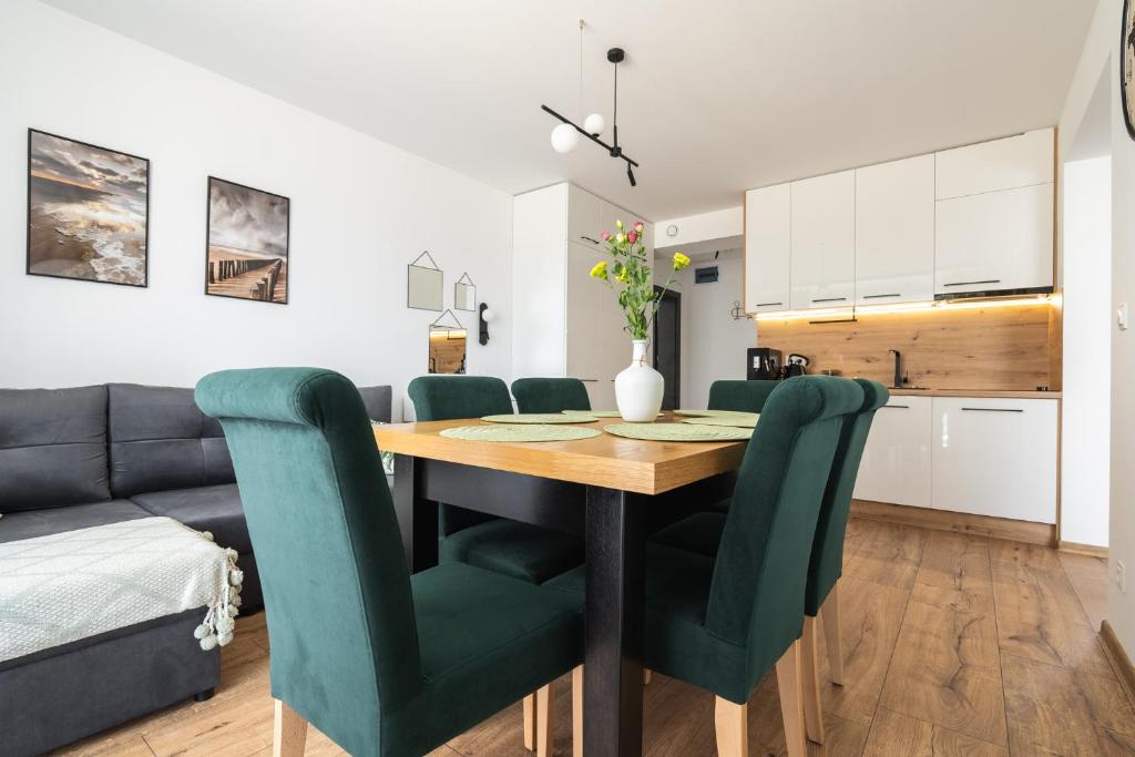 kuchnia i jadalnia z drewnianym stołem i zielonymi krzesłami w obiekcie SOLEK Apartamenty i pokoje gościnne w mieście Mielno