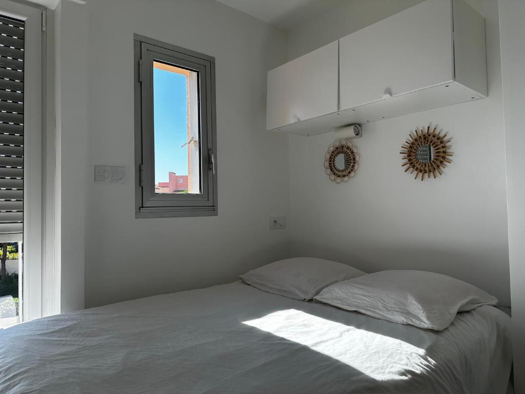 een witte slaapkamer met een bed en een raam bij STUDIO VUE PORT PISCINE PARKING in Cap d'Agde