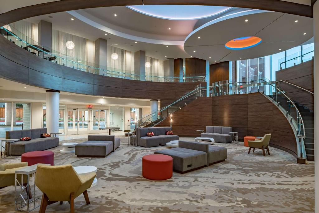 a lobby with a staircase with couches and chairs at Hilton Garden Inn Dallas At Hurst Conference Center in Hurst