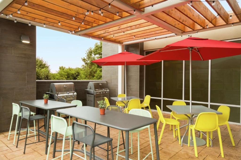 un patio con mesas, sillas y sombrillas rojas en Home2 Suites By Hilton Frederick en Frederick