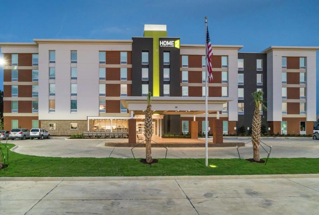 Home2 Suites By Hilton Jackson Flowood Airport Area في فلووود: مبنى الفندق مع العلم امامه