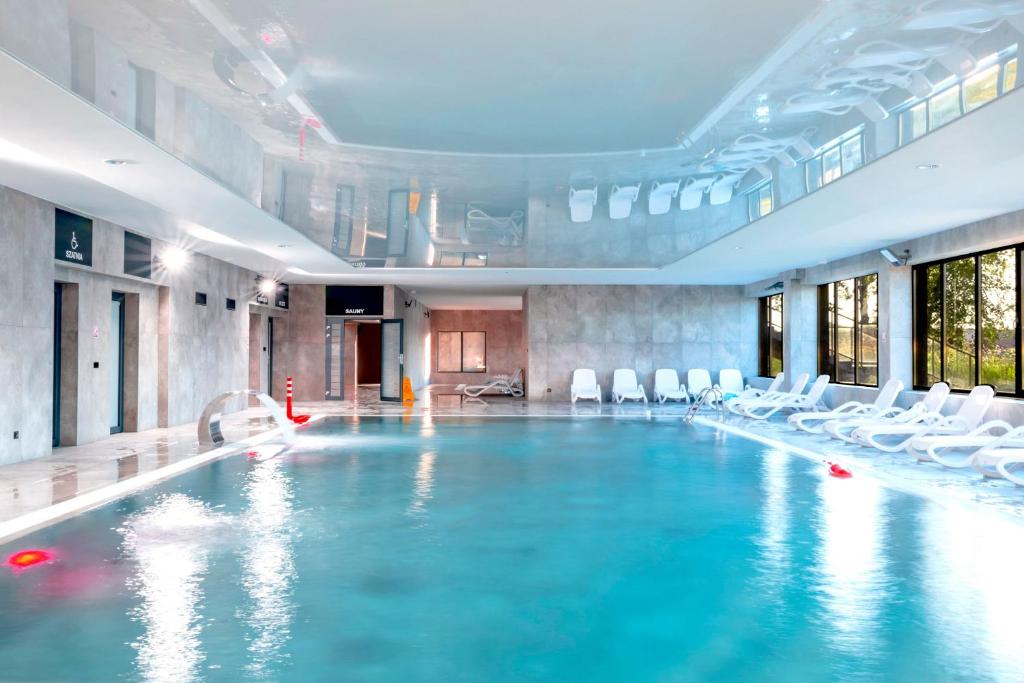a large swimming pool with white chairs in a building at Apartament Opal 34 Family & SPA in Dziwnów