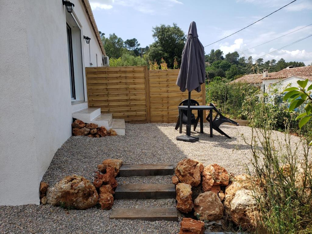um pátio com um banco, um guarda-chuva e pedras em Studio dans villa avec jardin em Le Thoronet