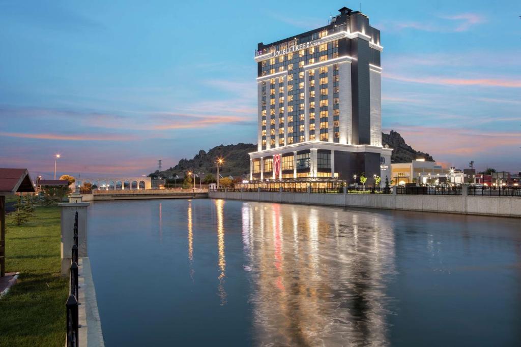 a tall building with a reflection in a body of water at Doubletree By Hilton Afyonkarahisar in Afyon