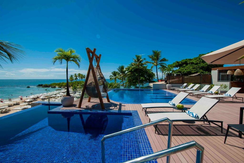 a resort swimming pool with lounge chairs and the ocean at Pousada Bahia Tambor in Morro de São Paulo