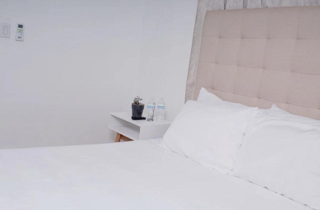 ein weißes Schlafzimmer mit einem weißen Bett und einem Nachttisch in der Unterkunft House Corner in San Pedro Sula