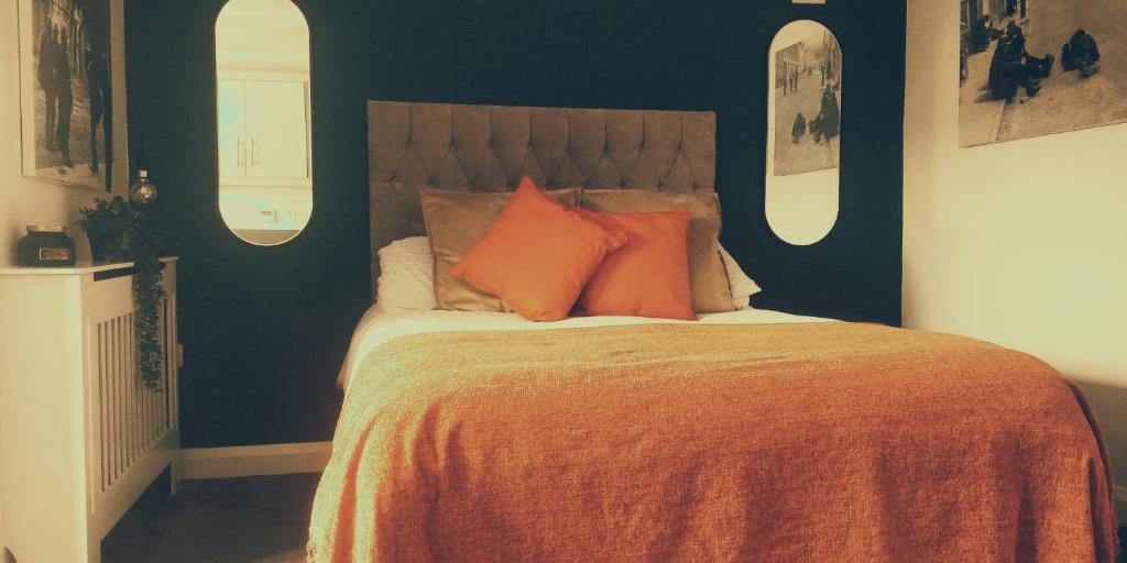 Free Derry Apartments في ديري لندنديري: غرفة نوم مع سرير ووسائد برتقالية عليه