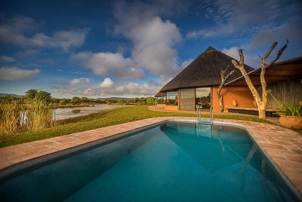a swimming pool in front of a building with a hut at Mount Etjo Safari Lodge in Kalkfeld