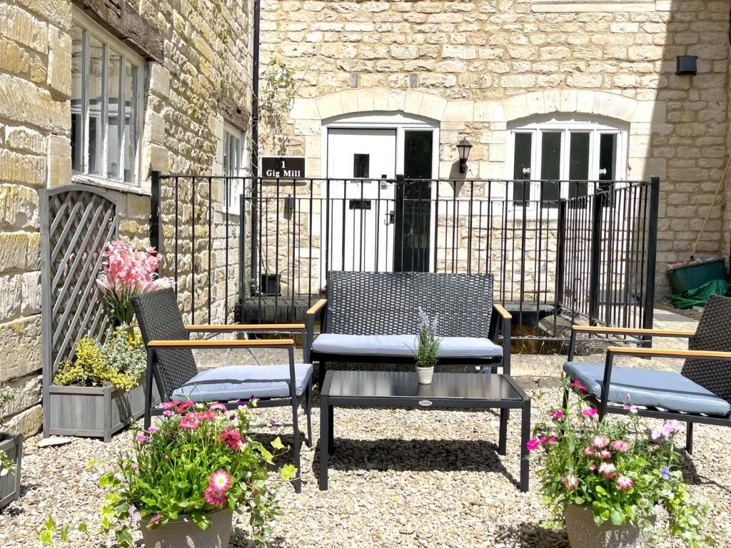 a patio with three chairs and a table with flowers at Lakeside Mill Cottage in Stroud
