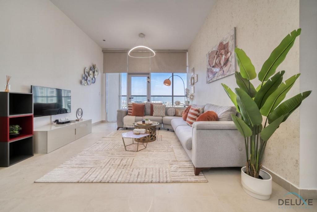 Pacific 1BR at Azizi Samia Jebel Ali by Deluxe Holiday Homes في دبي: غرفة معيشة مع أريكة ونبات الفخار