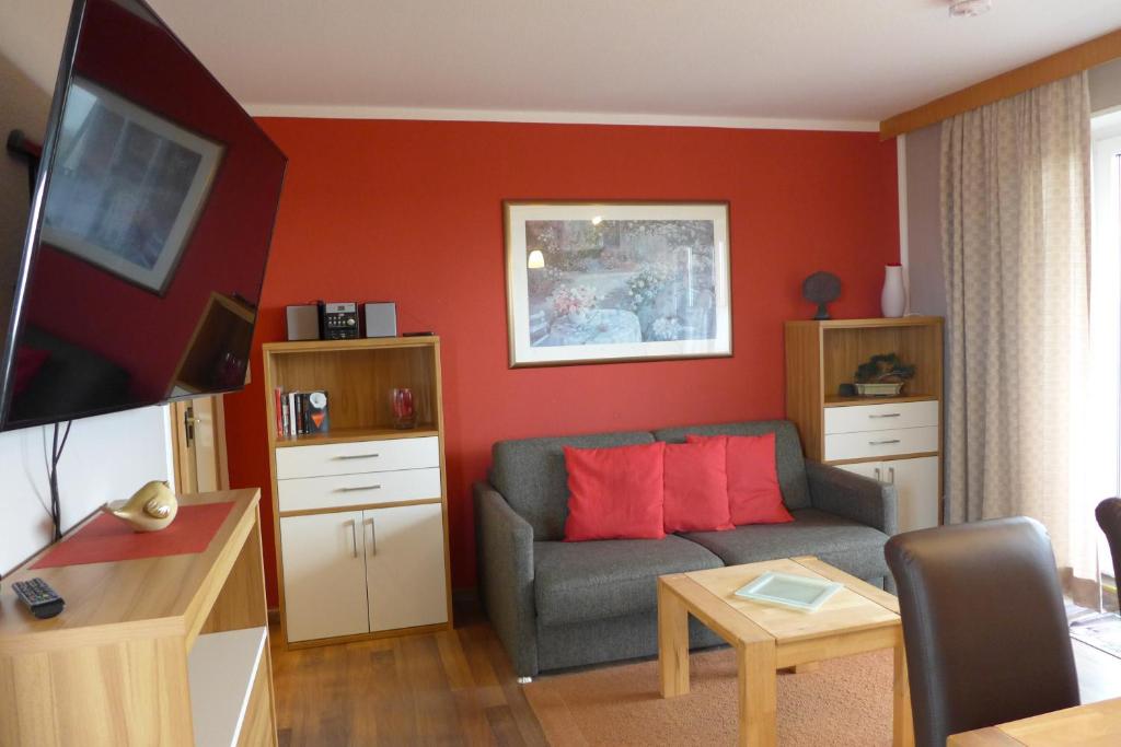 a living room with a couch and a red wall at Tief 10 Steuerbord 502 in Wangerland