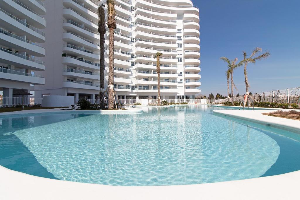 einem Pool vor einem großen Apartmenthaus in der Unterkunft Global Properties, Apartamento con terraza, vistas al mar y a la piscina in Canet d'en Berenguer