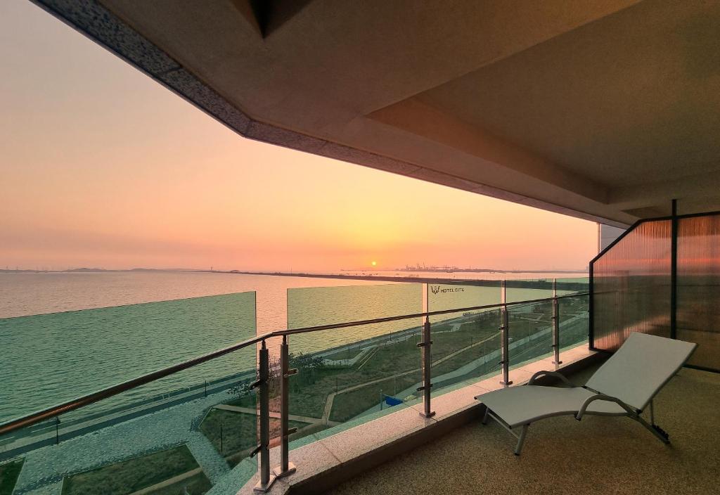 a balcony with a chair and the ocean at sunset at Hotel GITE in Siheung