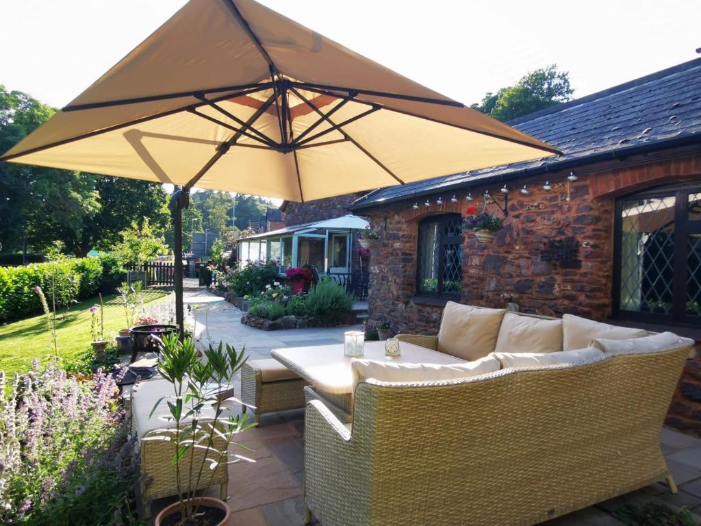 een patio met een bank en een parasol bij Luxury Cottage in Somerset in Wiveliscombe