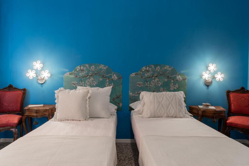 two beds in a room with blue walls and red chairs at Un tocco di Blu - La Vegra Apartment in Ferrara