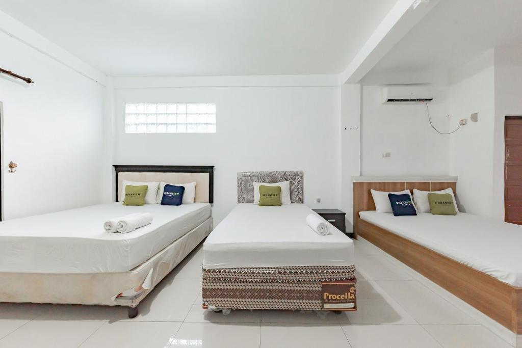 two beds in a room with white walls at Urbanview Hotel 99 Syariah Banjarbaru by RedDoorz in Martapura