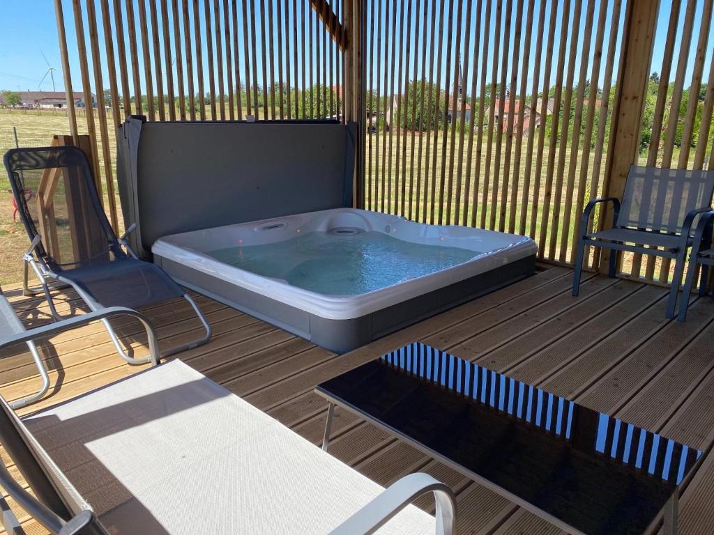 - un bain à remous installé sur une terrasse avec 2 chaises dans l'établissement Chalet avec spa, Au Bois Quartois, à La Quarte