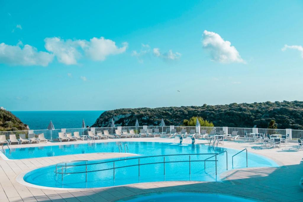 a swimming pool with chairs and the ocean in the background at Seth Playa Azul in Cala en Porter