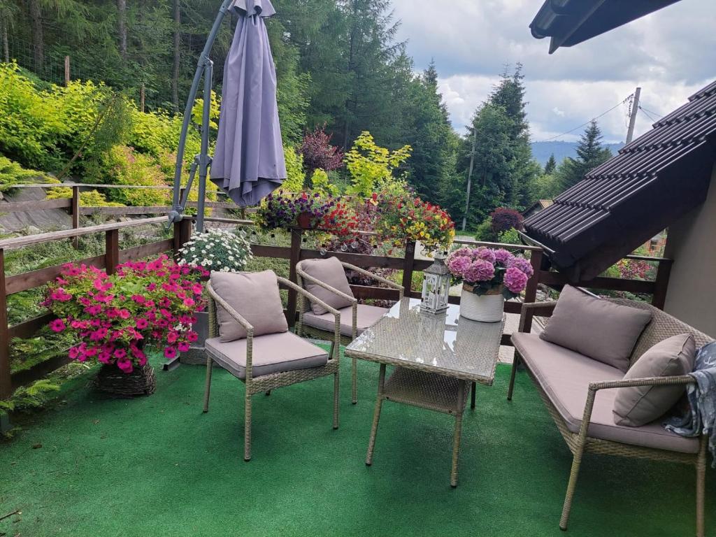 a patio with chairs and an umbrella and flowers at Apartamenty nad Strumykiem in Brenna
