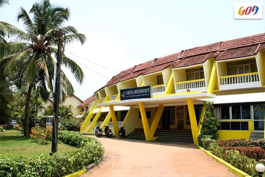 a hotel with a yellow building with a palm tree at Colva Residency in Colva