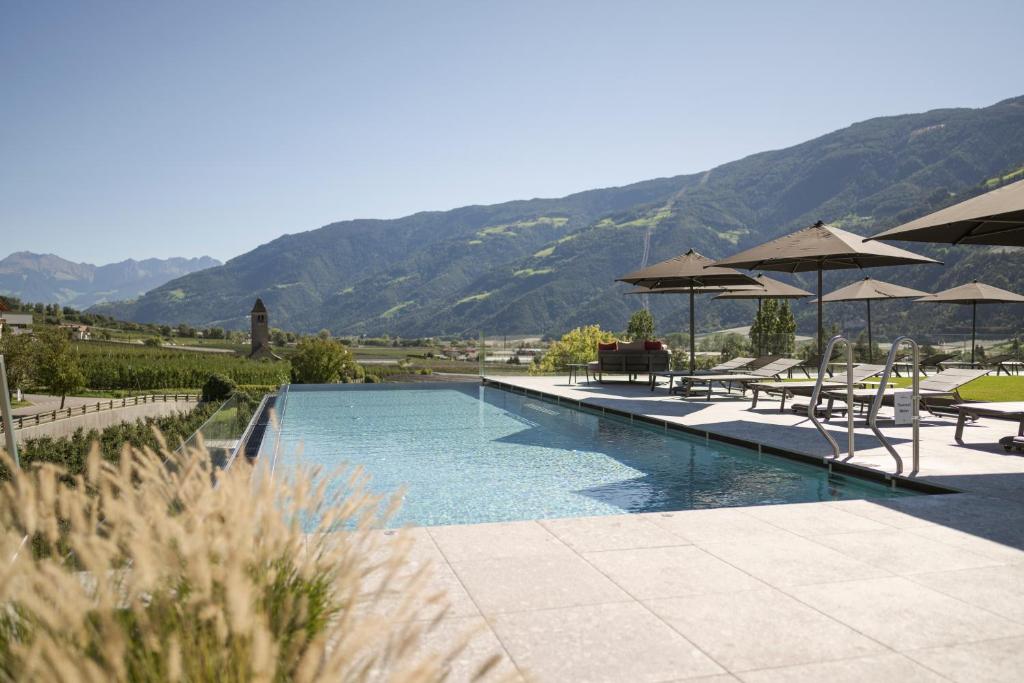 a swimming pool with tables and umbrellas and mountains at Feldhof DolceVita Resort in Naturno