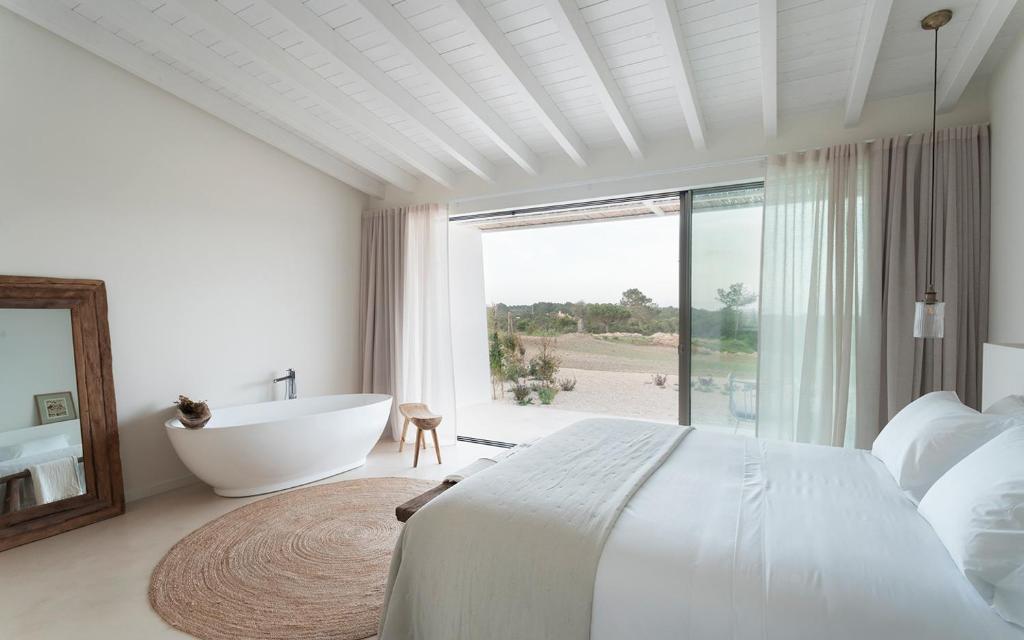 a white bedroom with a tub and a large window at Amaria in Aljezur
