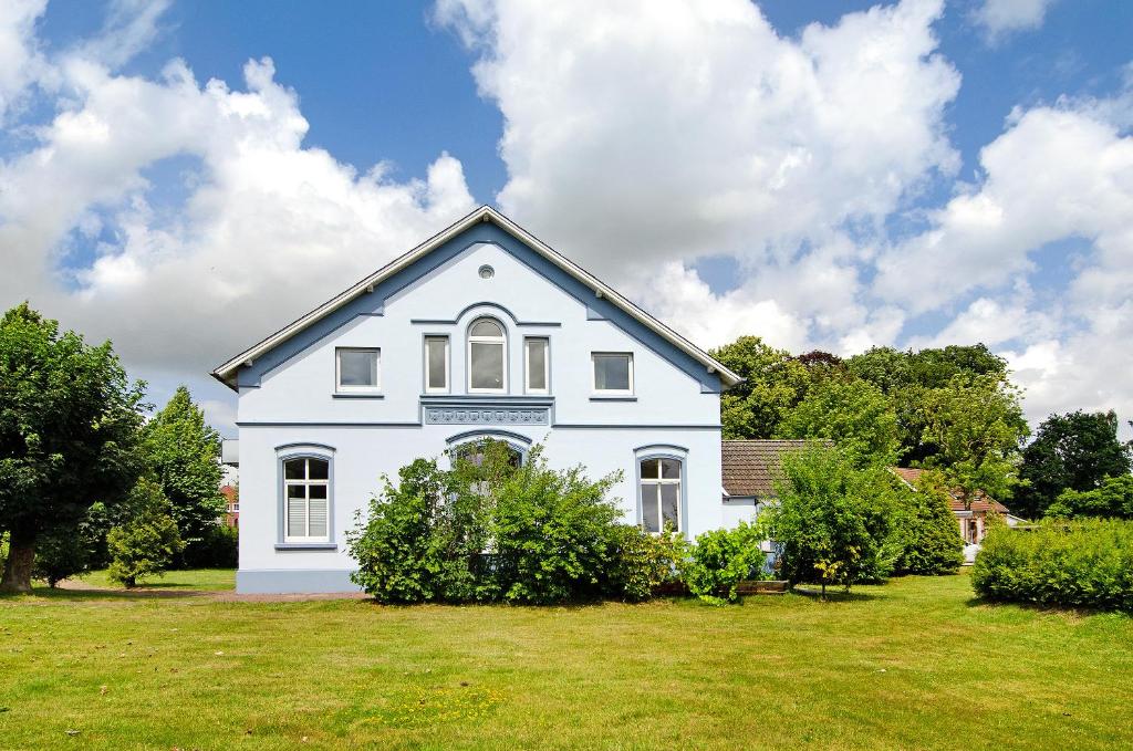 a white house on a grassy yard with trees at Villa Fokken Bootsmannsquartier in Esens