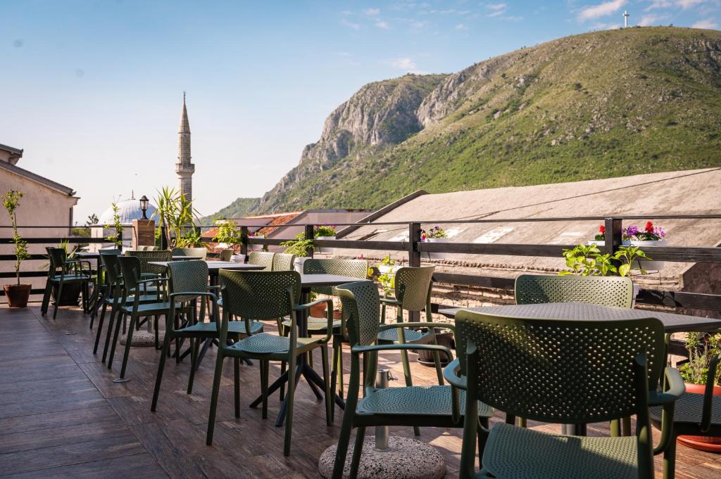 una fila de mesas y sillas en una terraza con una montaña en Hostel Backpackers, en Mostar