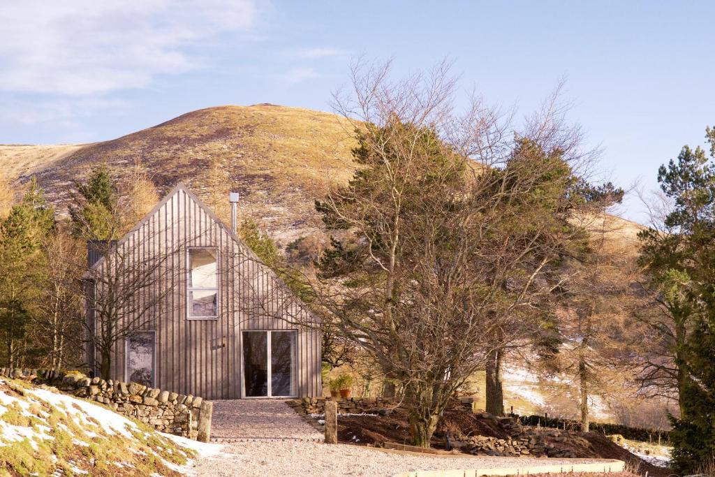 a wooden house in front of a mountain at Eastside Woodshed - Pentland cabin set in the hills near Edinburgh in Penicuik