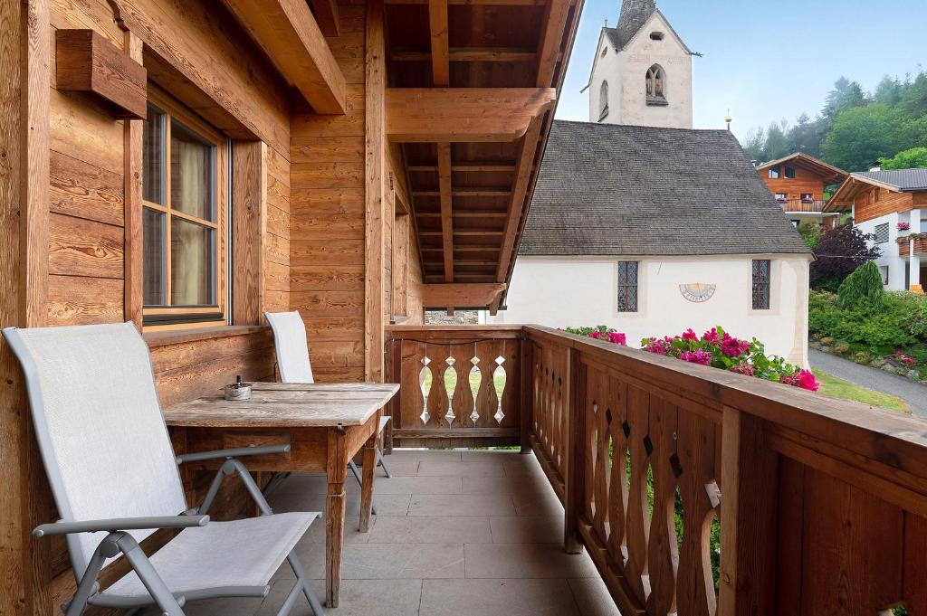 einen Holzbalkon mit einem Holztisch und einer Kirche in der Unterkunft Aurora Moarhof Natur Apartments in Lajen