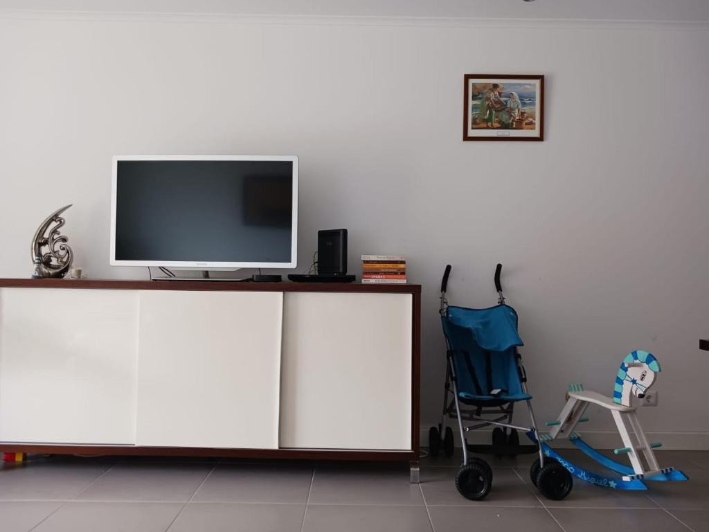 a tv on top of a cabinet with a blue chair at Mar & Praia - Apartamento Pedra Ouro in Pedra Do Ouro