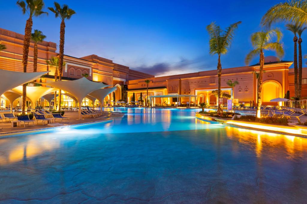 a large swimming pool with palm trees and buildings at Savoy Le Grand Hotel Marrakech in Marrakesh