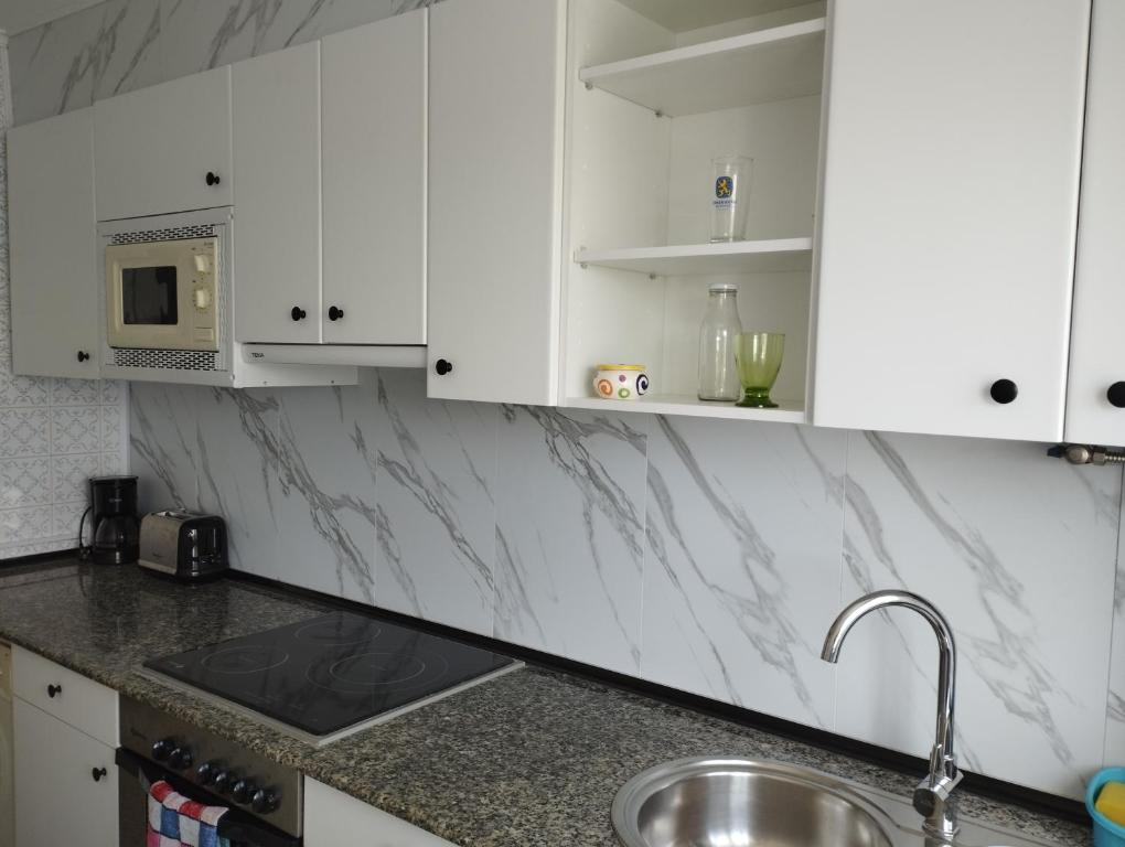 Una cocina con gabinetes blancos, un fregadero y un microondas. en Apartamento Vicsus, en Ajo