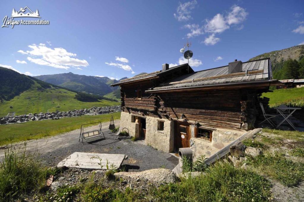 uma antiga casa de madeira numa colina com montanhas ao fundo em Chalet Heaven Mottolino em Livigno
