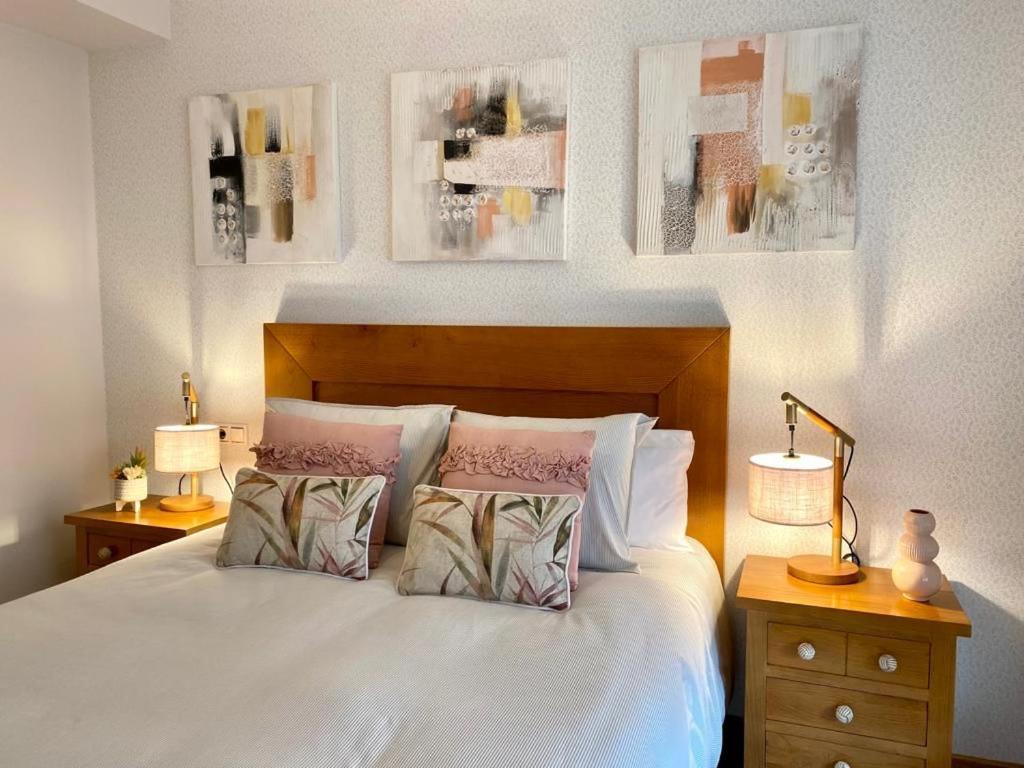 een slaapkamer met een wit bed met 2 lampen en foto's aan de muur bij Andainas Apartamentos Turísticos F in Milladoiro