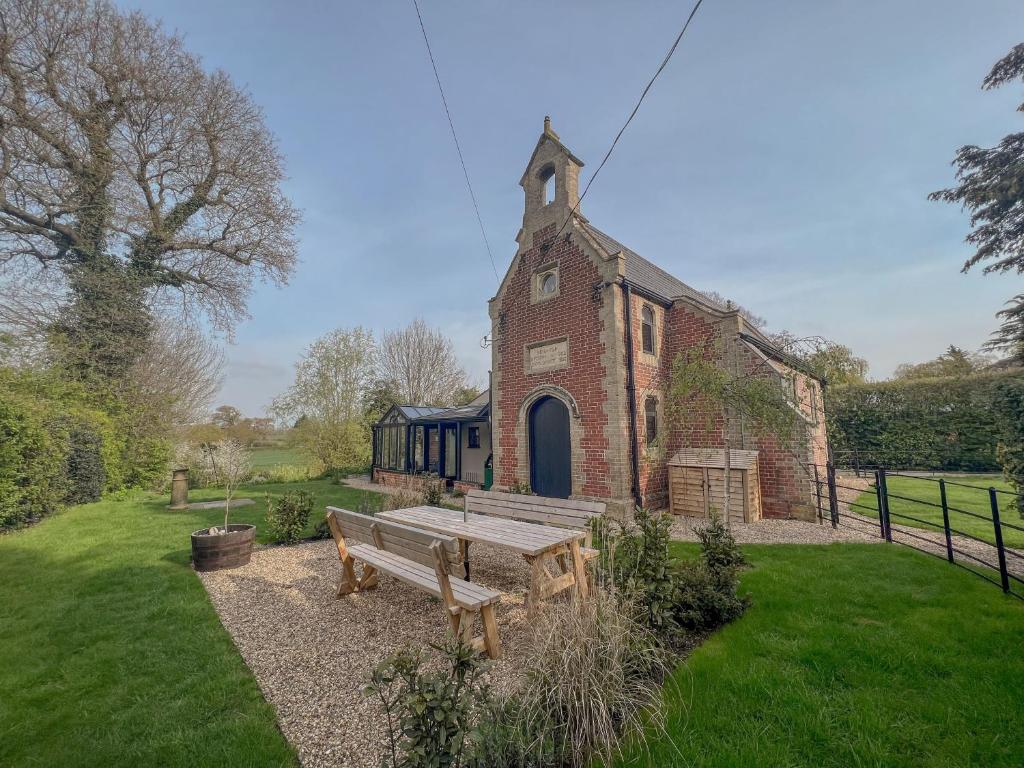 a wooden bench in front of a building with a church at Old School House - Luxury 4 bed holiday home near Norwich, Norfolk in Lingwood