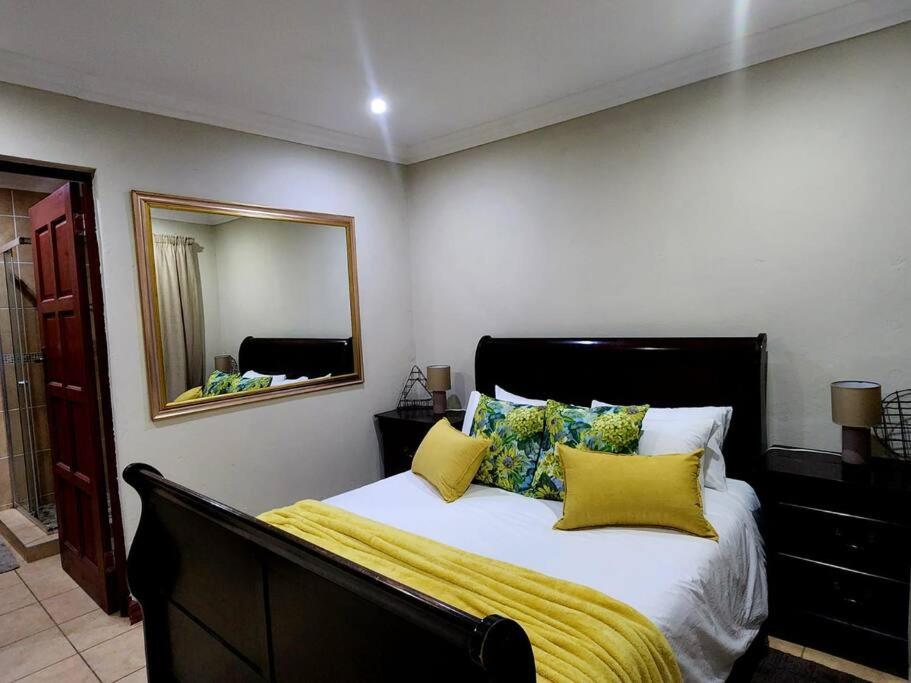 a bedroom with a bed with yellow pillows and a mirror at Lily Rest Garden Cottage in Pretoria