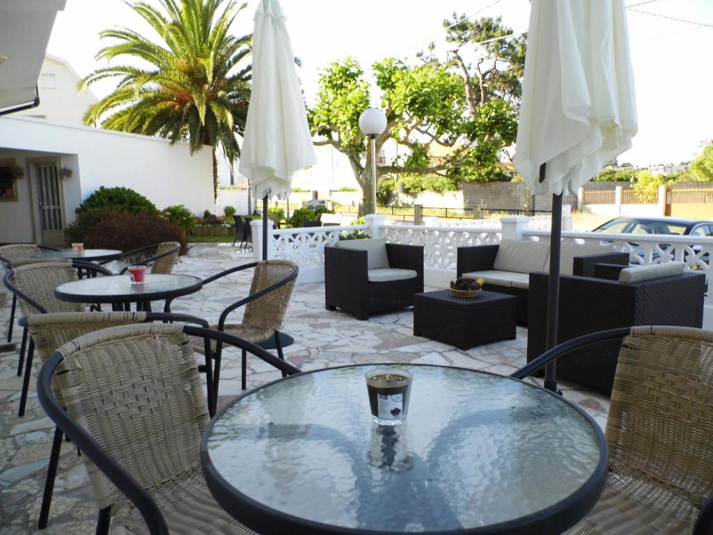 eine Terrasse mit Tischen, Stühlen und weißen Sonnenschirmen in der Unterkunft Hotel Arboleda in A Lanzada