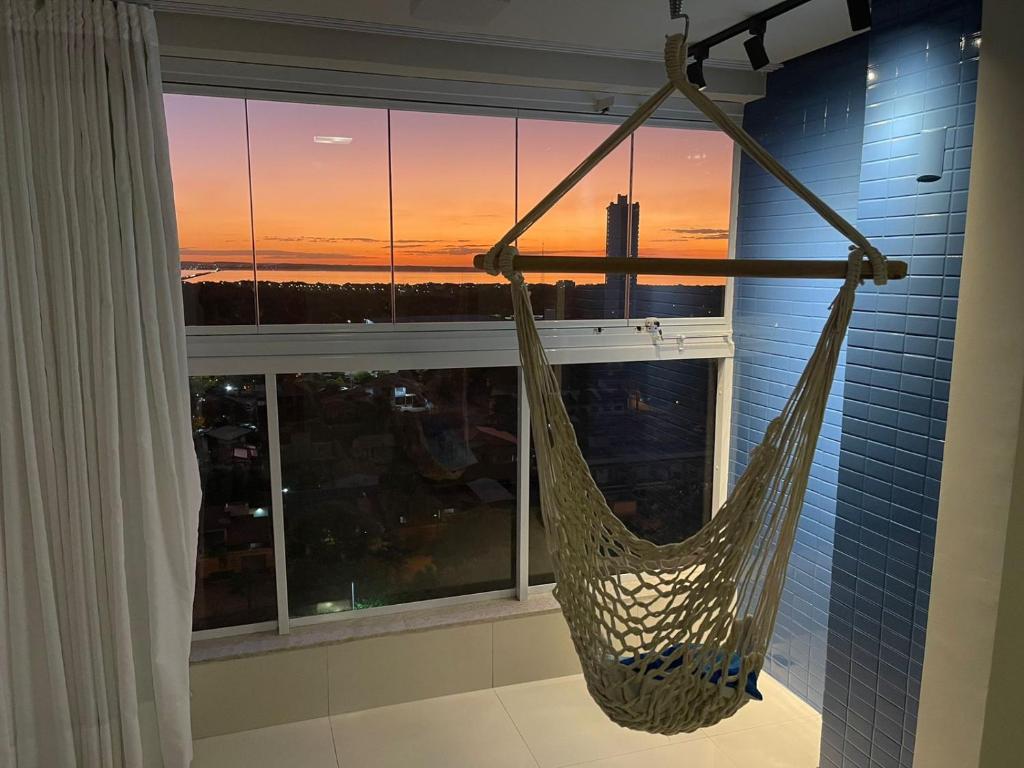 a hammock in a room with a window with a sunset at Apartamento Horizonte Azul, vista lago, próximo ao shopping in Palmas