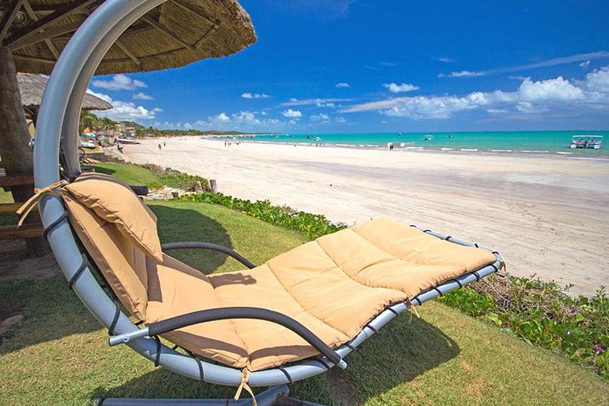 a beach chair sitting under an umbrella next to a beach at Pousada Portal do Maragogi in Maragogi