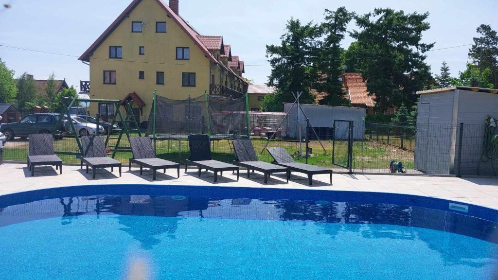 a swimming pool with chairs and a house in the background at Pokoje U Emilii in Kąty Rybackie