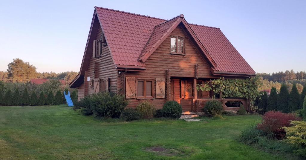 a wooden house with a red roof on a field at Najtańsze domki na Mazurach rezerwuj taniej tel 512-29O-43O rezerwacje tylko telefonicznie in Krutyń