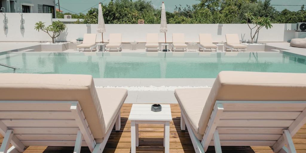 a swimming pool with white chairs and a table at Ennea Suites-Frost suite in Flámbouras